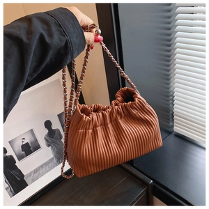 Detailed view of brown pleated cloud bucket bag with gold chain strap held by a person