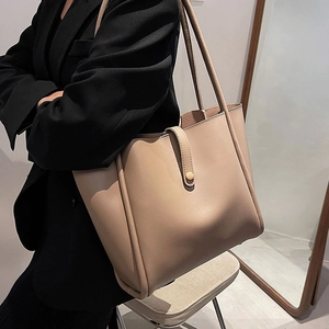 Minimalist beige leather tote bag with long straps shown on a model in a modern interior