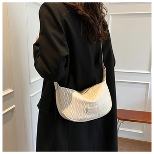Close-up of pleated cream half-moon crossbody bag with rectangular fashion plaque
