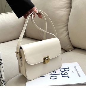 Gros plan d'un sac bandoulière rétro crème avec fermoir doré sur canapé chic
