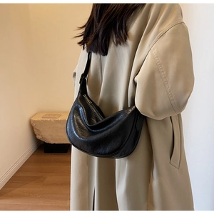 Detail of black pleated half-moon shoulder bag on model wearing a beige trench coat