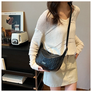 Close-up of black quilted dumpling bag with V-shaped pleats and metal brand plaque