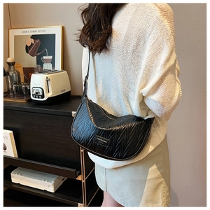 Detail of black pleated croissant bag with a glossy finish and fashion brand logo