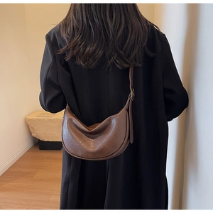 Brown faux leather crescent bag worn by a model in a minimalist indoor setting