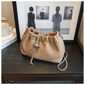 Detailed macro view of beige pleated bucket bag texture with silver chain and metal orb charm