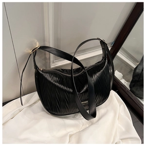 Close-up of black pleated dumpling bag with adjustable strap and silver logo plaque