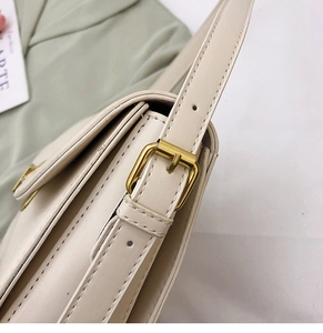 Détail de la boucle dorée réglable sur un sac bandoulière en cuir beige avec coutures fines