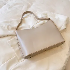 Detail view of beige leather tote bag with protective metal feet on a smooth base