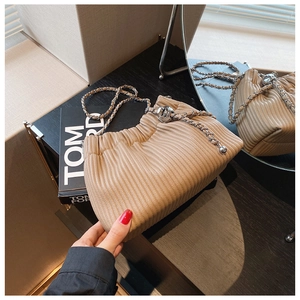 Detailed view of beige pleated bucket bag with silver chain strap and metal ball decor