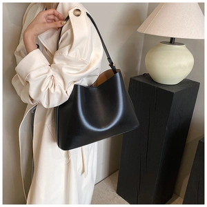 Detail of a minimalist black leather tote bag worn by a model in a beige trench coat