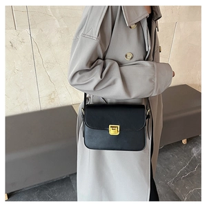 Dettaglio borsa a tracolla in pelle nera con chiusura dorata su trench grigio elegante