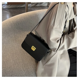 Dettaglio di una borsa a tracolla nera con fibbia dorata su un cappotto beige classico