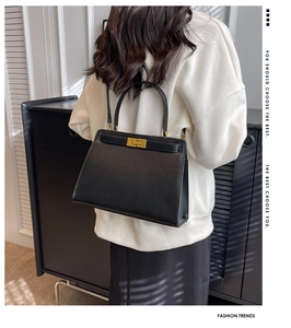 Detail of elegant black leather shoulder bag with gold clasp shown on a model