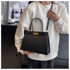 Detail of a black structured leather bag featuring a vintage matte gold clasp and handle