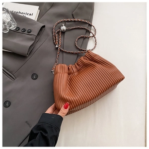 Brown pleated bucket bag with silver chain and metal ball detail on a grey blazer