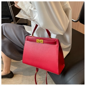 Detail of red leather crossbody Kelly bag shown on a model with golden clasp and strap