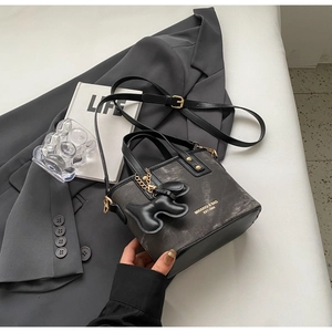 Detail of grey vintage tote bag with puppy charm on dark blazer and prop book