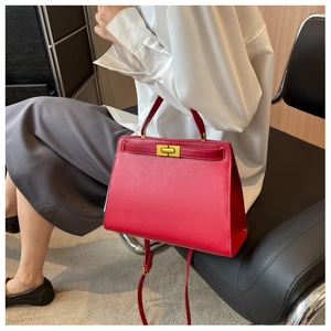 Detail of red leather Kelly bag with golden twist lock and textured finish in use