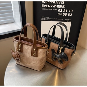Detailed close-up of suede tote bags with leather trim and gold animal charms