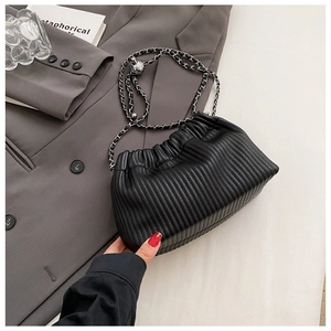 Detail of black pleated cloud bucket bag with silver chain strap on a blazer background