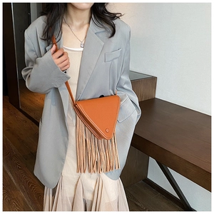 Détail du sac bandoulière triangle orange vif à franges sur un mannequin en blazer gris