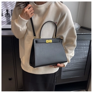 Detail of a black trapezoid crossbody bag with gold-tone hardware on a model