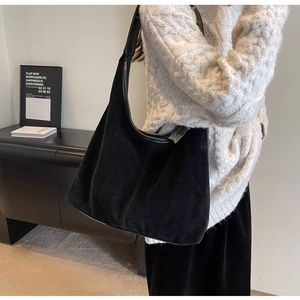 Detail of a large black suede tote bag shown on a model in a minimalist home setting