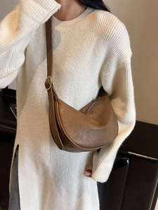 Brown leather crescent crossbody bag with adjustable strap and gold buckles on a model