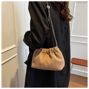 Detail of a beige pleated cloud bag with silver chain strap worn over a black blazer
