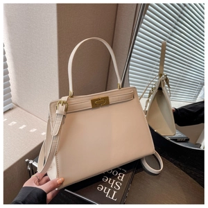 Detailed view of cream trapezoid handbag with gold-tone hardware on dark wood surface
