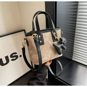 Detail of a beige tote bag featuring black leather trim and a cute dog-shaped charm