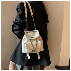 Close-up of a white quilted mini backpack with silver chain straps on a model in a suit