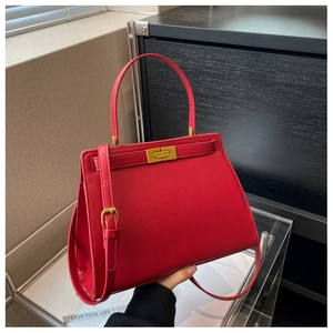 Detail of red leather Kelly bag featuring a gold turn-lock and adjustable shoulder strap