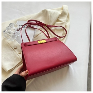 Detail of red leather trapezoid handbag with gold turn-lock and adjustable shoulder strap
