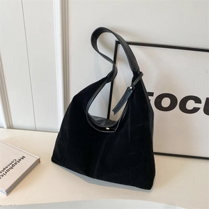 Minimalistische schwarze Hobo-Tasche aus Wildleder und Leder auf weißem Schreibtisch