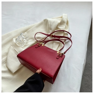 Detail of burgundy trapezoid leather handbag with gold hardware on beige blazer