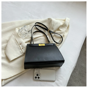 Detail of black leather handbag with gold twist lock on stylish tweed jacket background