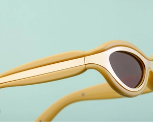 Dettaglio di piccoli occhiali da sole cat-eye con montatura gialla e intarsi in oro