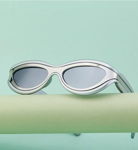 Occhiali da sole cat-eye argento futuristici con lenti grigie su espositore verde