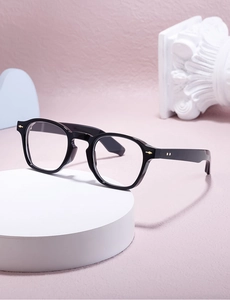 Detail of black acetate round glasses frame featuring gold arrow hinges and metal rivets