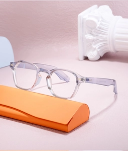 Close-up of translucent grey round glasses frame with orange leather case on a texture base