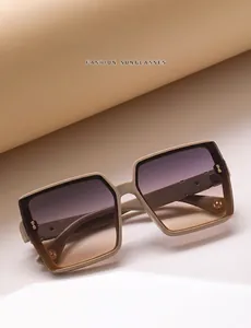 Detail van een vierkante beige zonnebril met kleurverloopglazen en gouden ornamenten