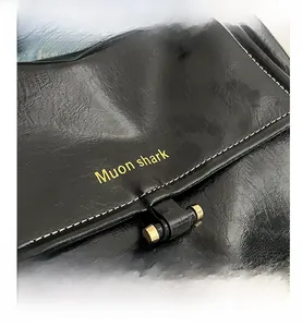 Detail of black lychee texture leather bag with white stitching and gold brand logo