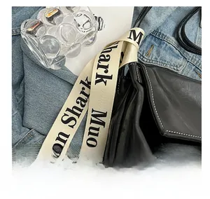 Detail of black glossy leather crossbody bag with white stitched edges and letter strap