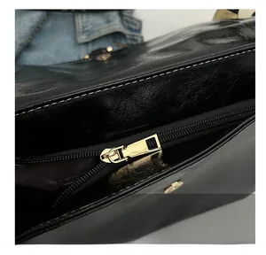 Detail of smooth golden zipper and magnetic buckle on black glossy shoulder bag