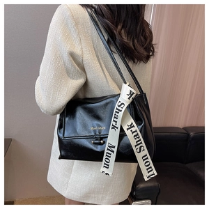 Close-up of black glossy shoulder bag with golden logo and stylish lettered strap details