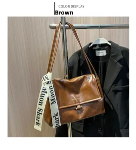 Detail of a brown leather shoulder bag featuring a metal lock and decorative logo ribbon