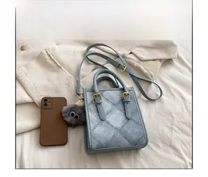 Detail of light blue denim-textured handbag with gold logo and grey fluffy keychain