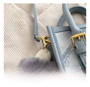 Detail view of light blue denim bag with golden hardware hooks and grey plush charm