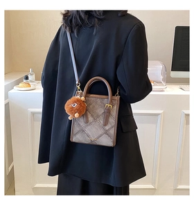 Detail view of the brown textured crossbody bag with a cute plush charm on model